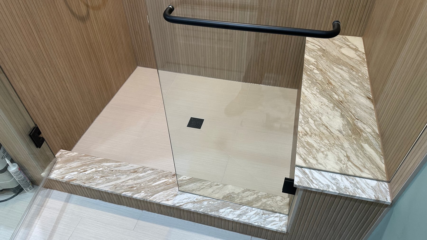 Completed modern tile shower floor repair in Highland Park, Illinois, with preserved wood-look walls, stone bench, black fixtures and glass enclosure